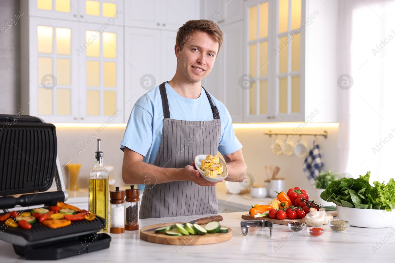 Photo of Man cooking vegetables on electric grill in kitchen