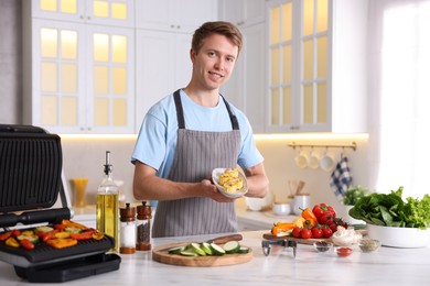 Photo of Man cooking vegetables on electric grill in kitchen