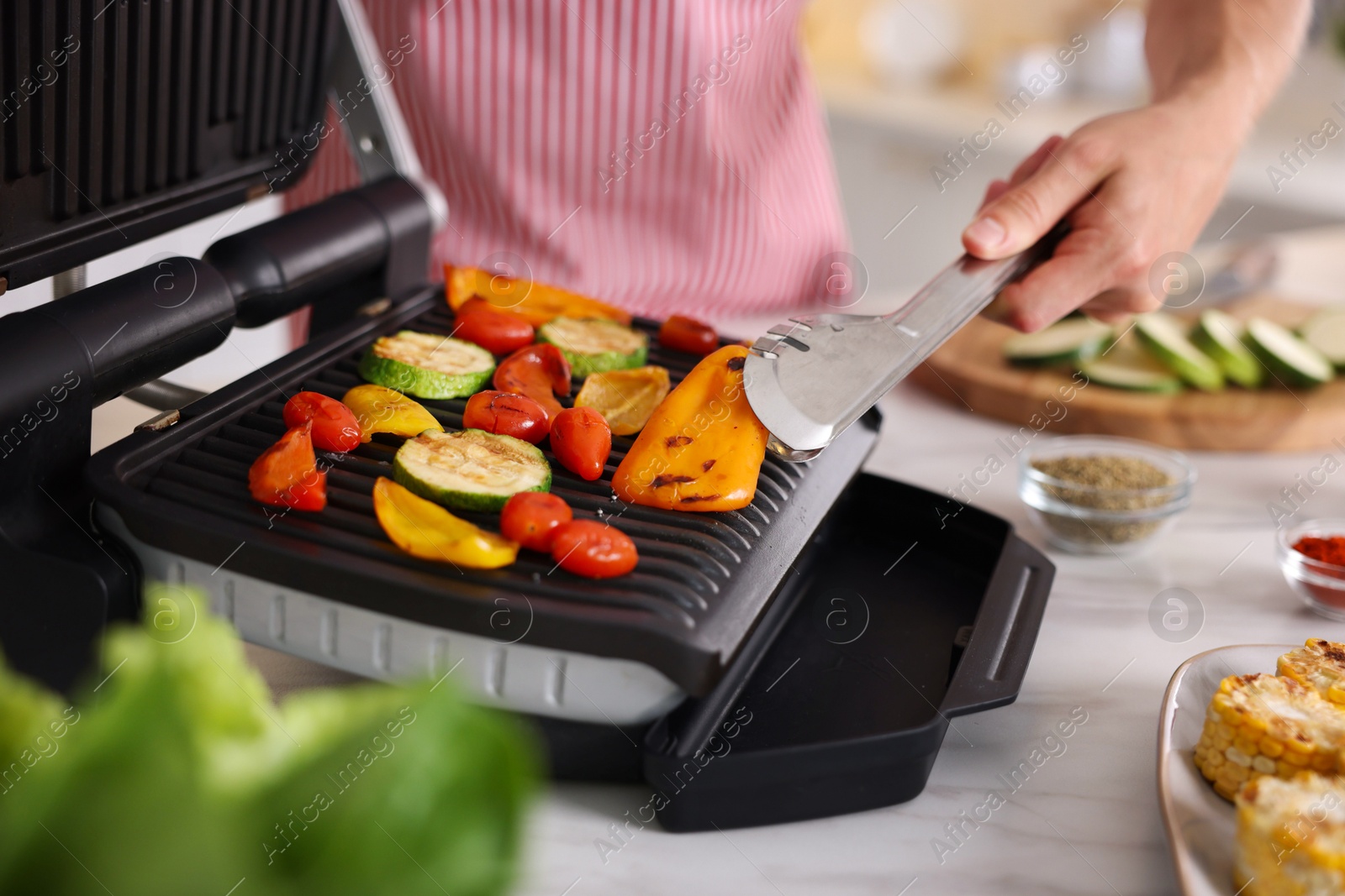 Photo of Man cooking vegetables on electric grill in kitchen, closeup