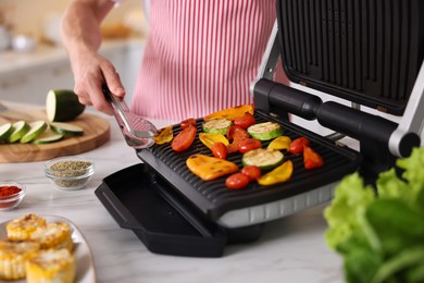 Photo of Man cooking vegetables on electric grill in kitchen, closeup