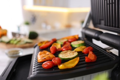 Photo of Electric grill with different vegetables on white table in kitchen, closeup