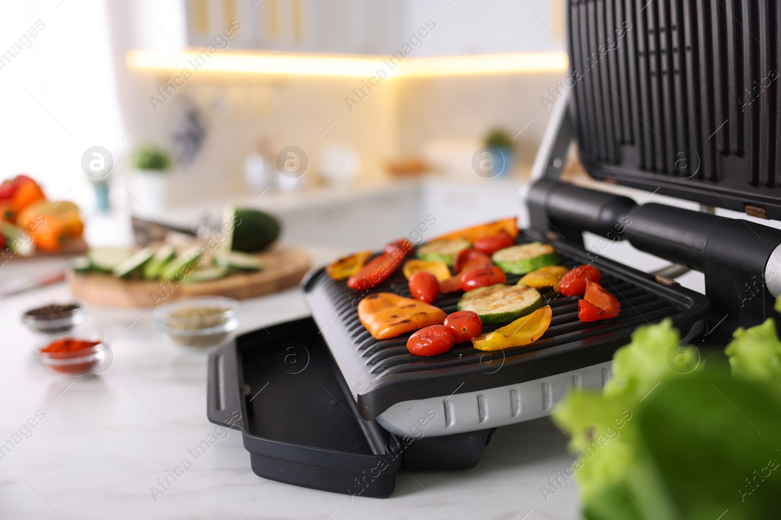 Photo of Electric grill with different vegetables on white table in kitchen, closeup