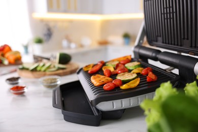 Photo of Electric grill with different vegetables on white table in kitchen, closeup