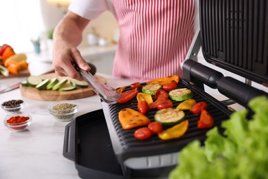 Photo of Man cooking vegetables on electric grill in kitchen, closeup