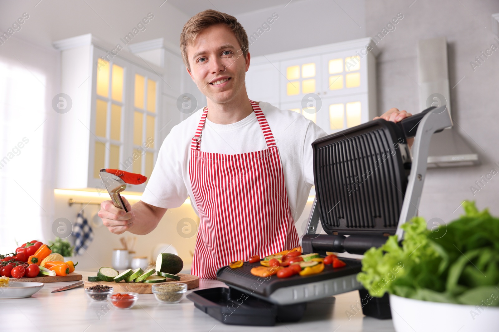 Photo of Man cooking vegetables on electric grill in kitchen