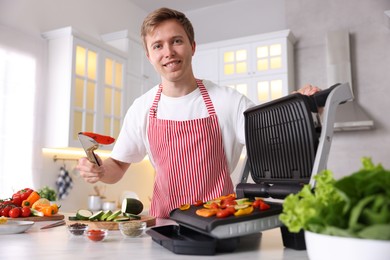 Photo of Man cooking vegetables on electric grill in kitchen