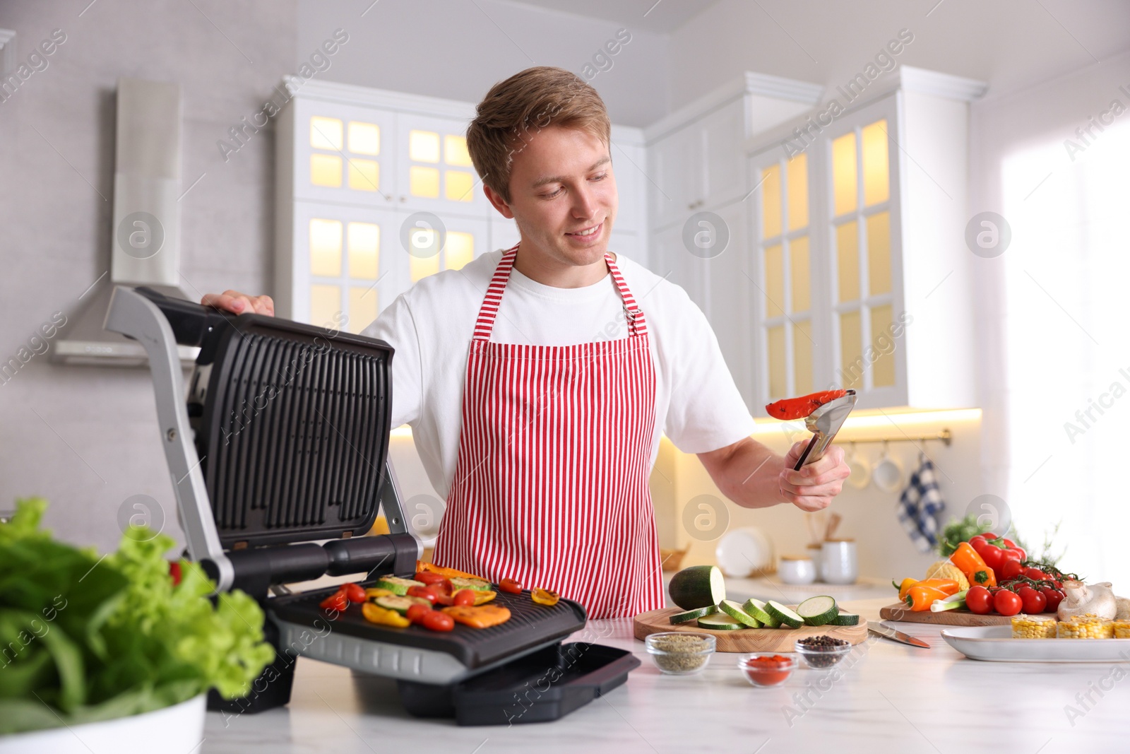 Photo of Man cooking vegetables on electric grill in kitchen
