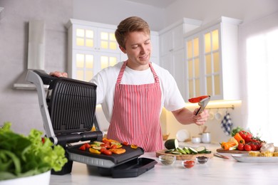 Photo of Man cooking vegetables on electric grill in kitchen