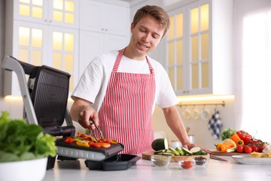 Photo of Man cooking vegetables on electric grill in kitchen