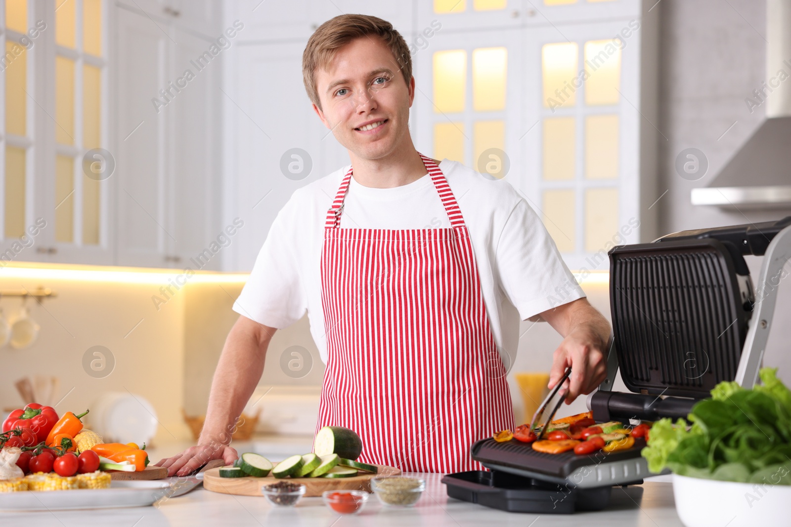 Photo of Man cooking vegetables on electric grill in kitchen
