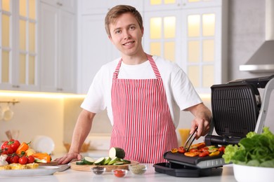 Photo of Man cooking vegetables on electric grill in kitchen