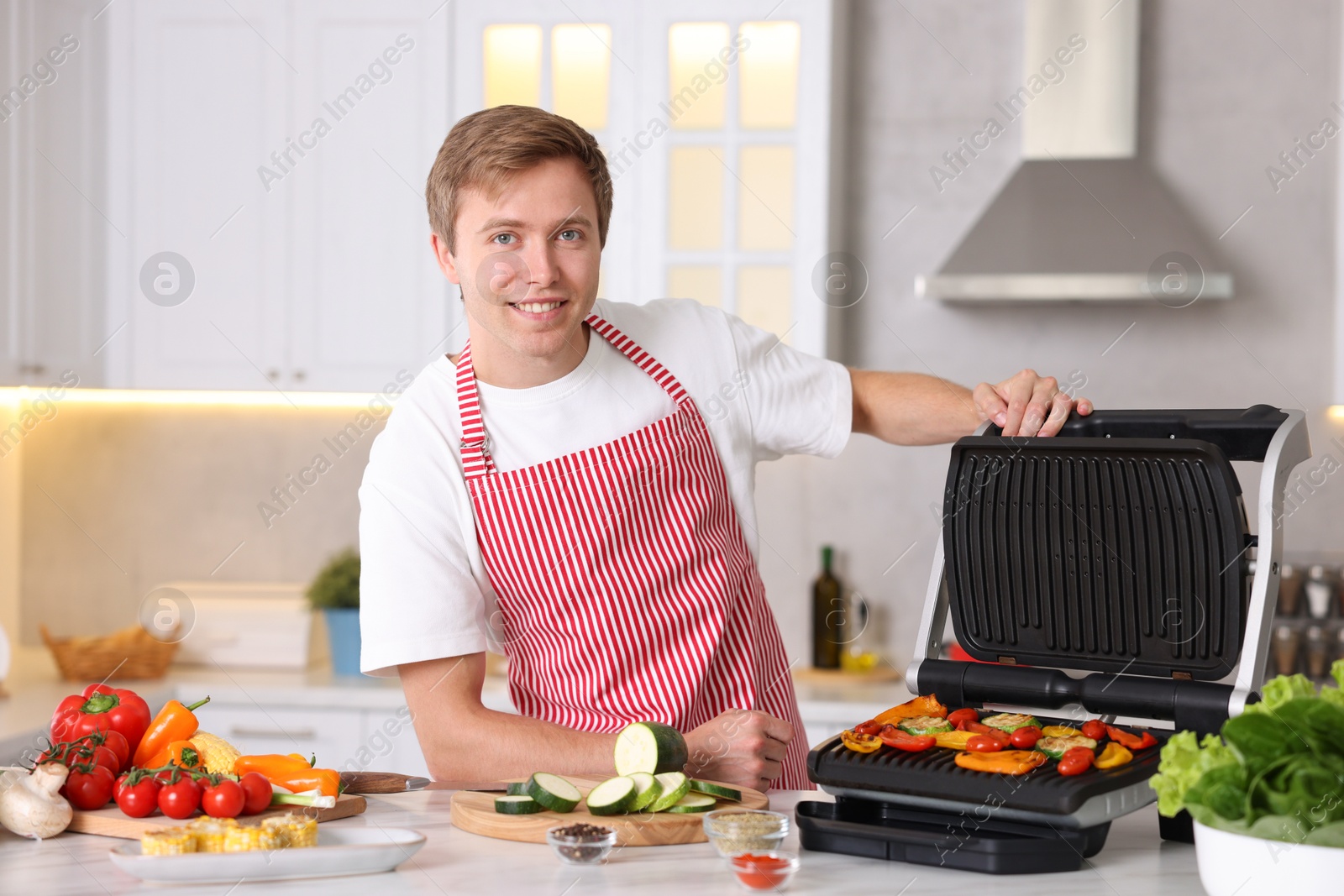Photo of Man cooking vegetables on electric grill in kitchen