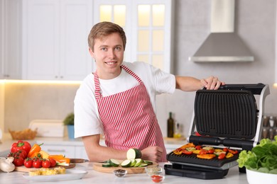 Photo of Man cooking vegetables on electric grill in kitchen