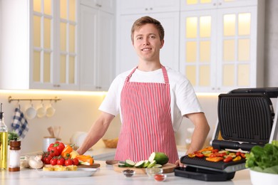 Photo of Man cooking vegetables on electric grill in kitchen