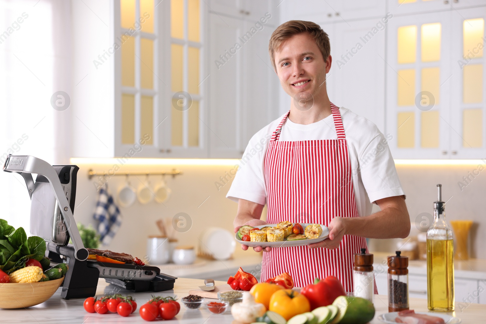 Photo of Man cooking vegetables on electric grill in kitchen