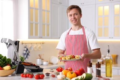 Photo of Man cooking vegetables on electric grill in kitchen