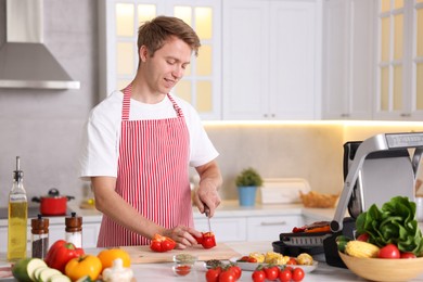 Photo of Man cutting pepper while cooking vegetables on electric grill in kitchen