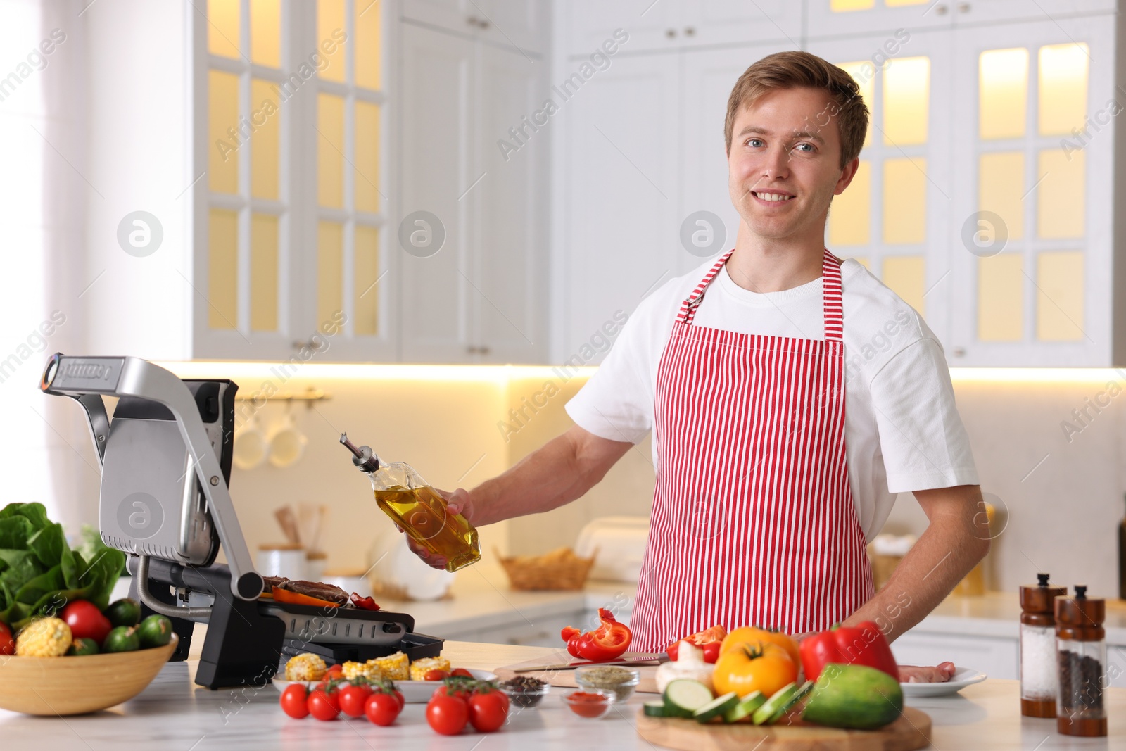 Photo of Man cooking meat and vegetables on electric grill in kitchen