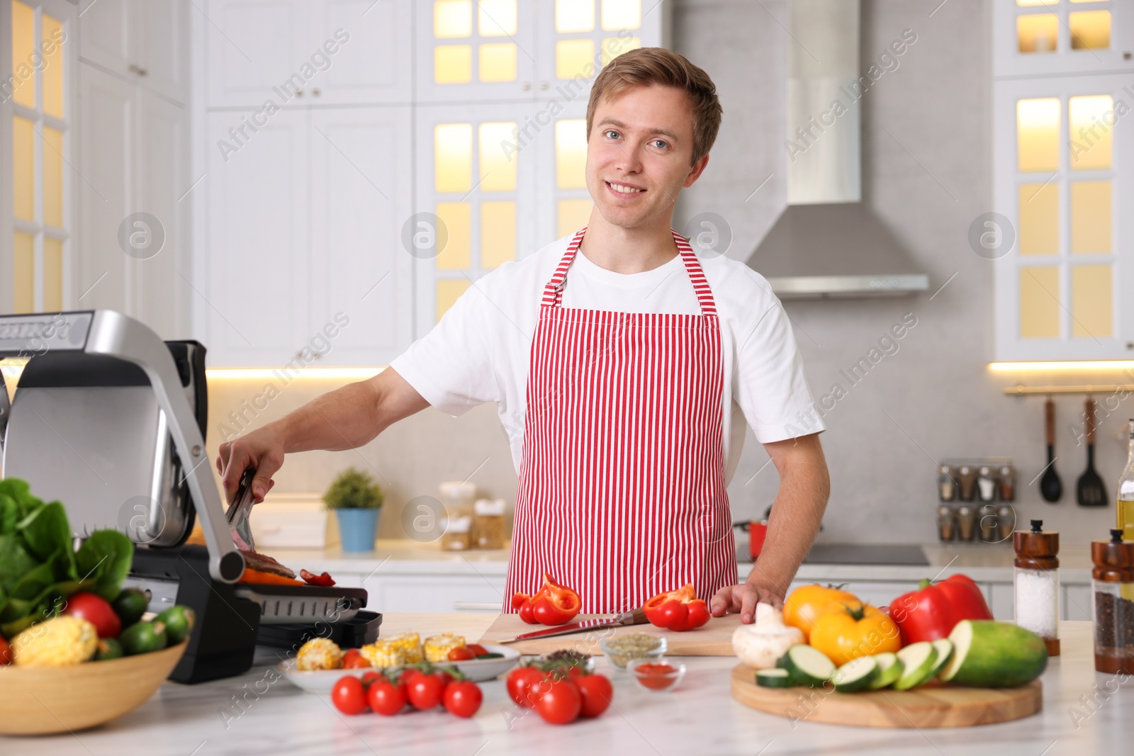Photo of Man cooking meat and vegetables on electric grill in kitchen