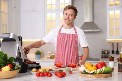 Photo of Man cooking meat and vegetables on electric grill in kitchen
