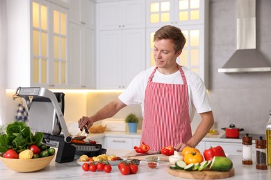 Photo of Man cooking meat and vegetables on electric grill in kitchen
