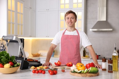 Photo of Man cooking meat and vegetables on electric grill in kitchen