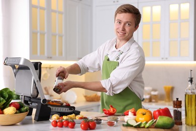 Photo of Man adding salt to vegetables and meat cooking on electric grill in kitchen