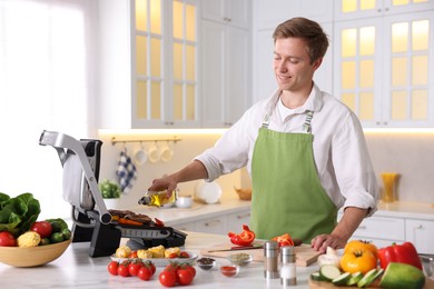 Photo of Man pouring oil onto vegetables cooking on electric grill in kitchen