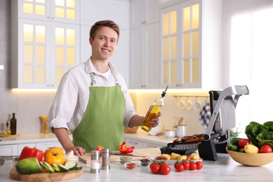 Photo of Man pouring oil onto vegetables cooking on electric grill in kitchen
