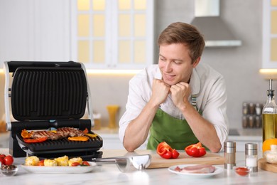 Photo of Man cooking meat and vegetables on electric grill in kitchen
