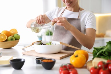 Photo of Cooking process. Smiling woman pouring oil onto salad at table indoors, closeup
