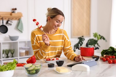 Photo of Cooking process. Smiling woman with skewer using tablet at table in kitchen