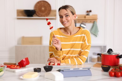 Photo of Smiling woman with tasty skewers after cooking at table in kitchen