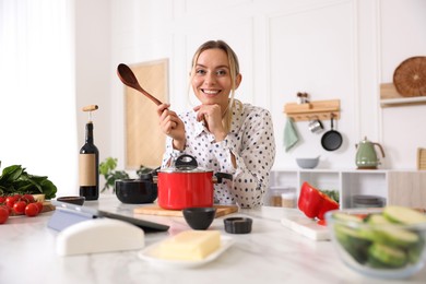 Photo of Portrait of smiling woman with spoon cooking at table in kitchen