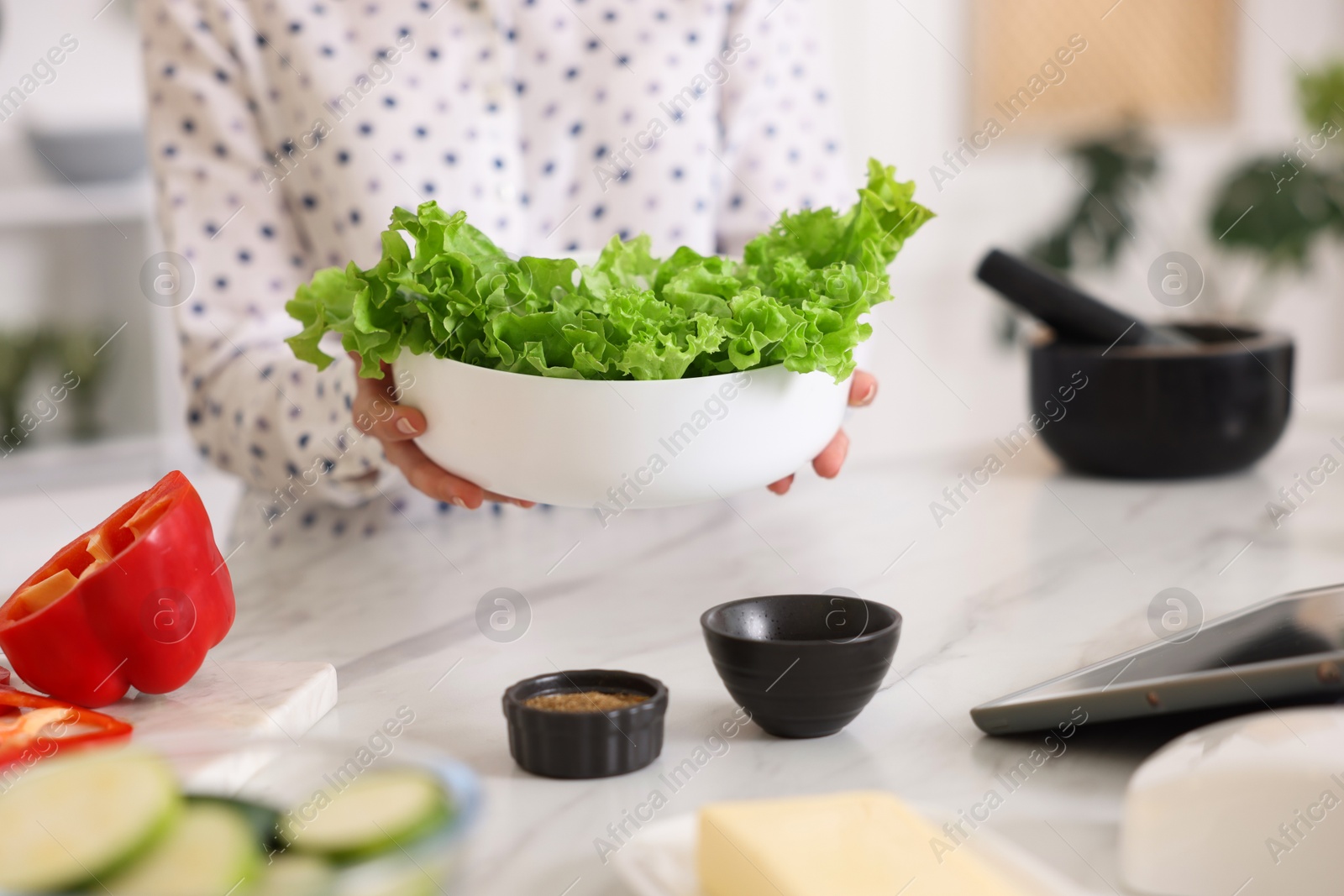 Photo of Cooking process. Woman with bowl of lettuce at marble table indoors, closeup