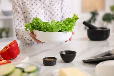 Photo of Cooking process. Woman with bowl of lettuce at marble table indoors, closeup