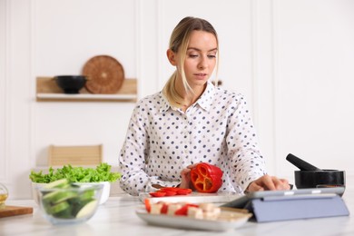 Photo of Beautiful woman looking at recipe on tablet while cooking at table in kitchen