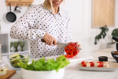 Photo of Cooking process. Smiling woman cutting bell pepper at table in kitchen, closeup