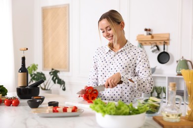 Photo of Cooking process. Smiling woman cutting bell pepper at table in kitchen