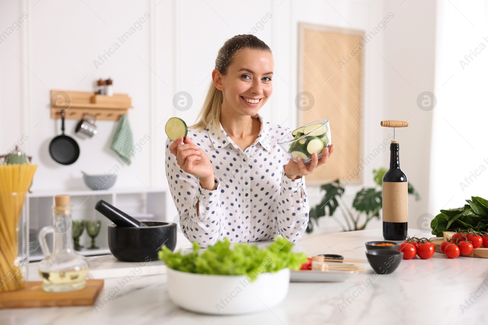 Photo of Portrait of smiling woman with slices of zucchini cooking at table in kitchen