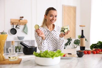 Photo of Portrait of smiling woman with slices of zucchini cooking at table in kitchen