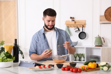 Photo of Cooking process. Young man seasoning dish at table in kitchen