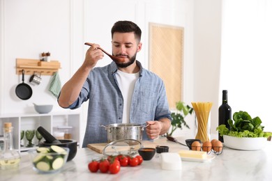 Photo of Young man tasting meal after cooking at table in kitchen