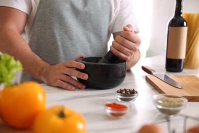 Photo of Man with mortar cooking at table indoors, closeup