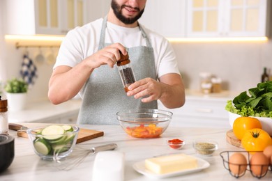 Photo of Cooking process. Smiling man seasoning dish at table in kitchen, closeup
