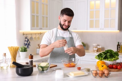 Photo of Cooking process. Smiling man seasoning dish at table in kitchen