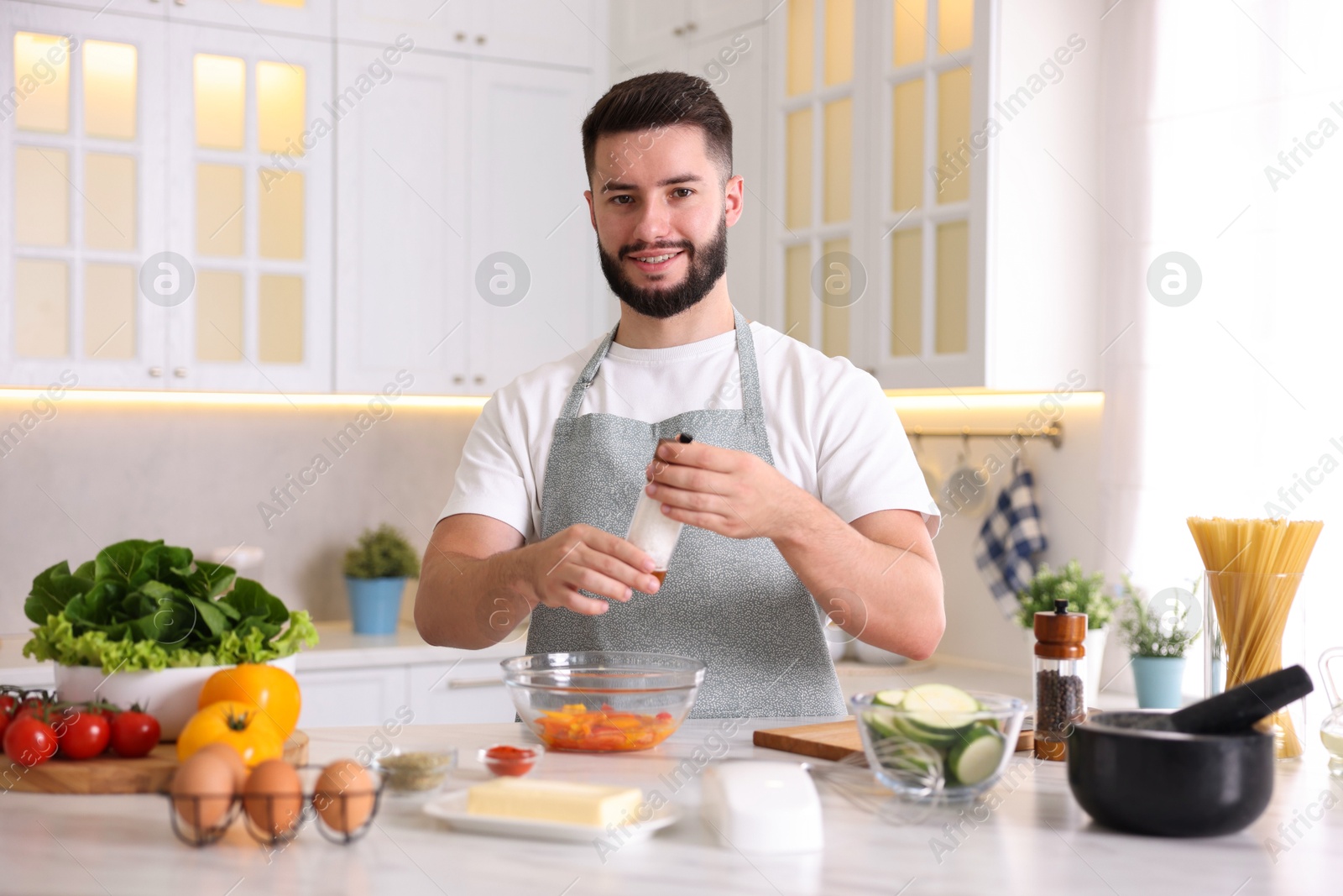 Photo of Cooking process. Smiling man seasoning dish at table in kitchen