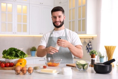 Photo of Cooking process. Smiling man seasoning dish at table in kitchen