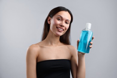 Photo of Smiling young woman with bottle of mouthwash on grey background. Oral hygiene