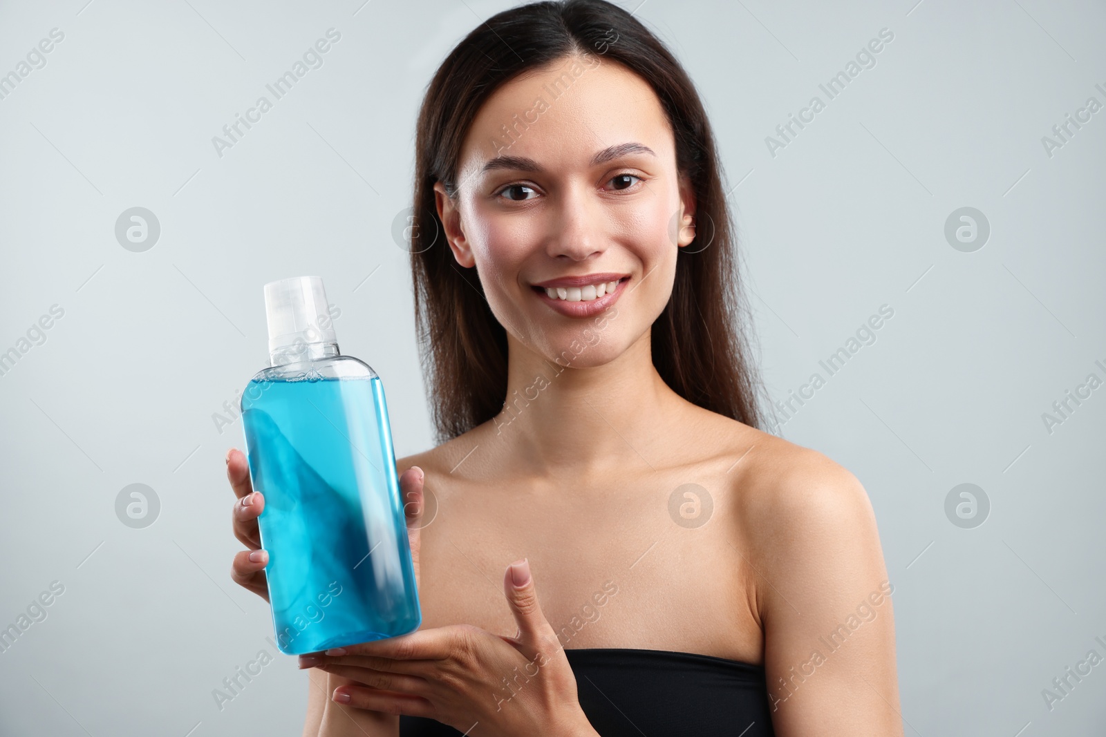 Photo of Smiling young woman with bottle of mouthwash on grey background. Oral hygiene